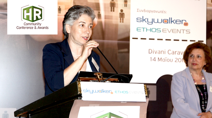 Representative of Psimiti AE talking on the podium, with a second person standing in the back